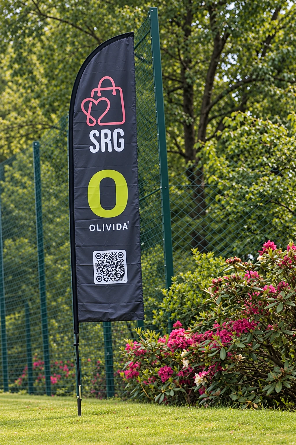 Eksempel på levering i dag: svart beachflagg med SRG- og Olivida-logo og QR-kode, utendørs i grønne omgivelser